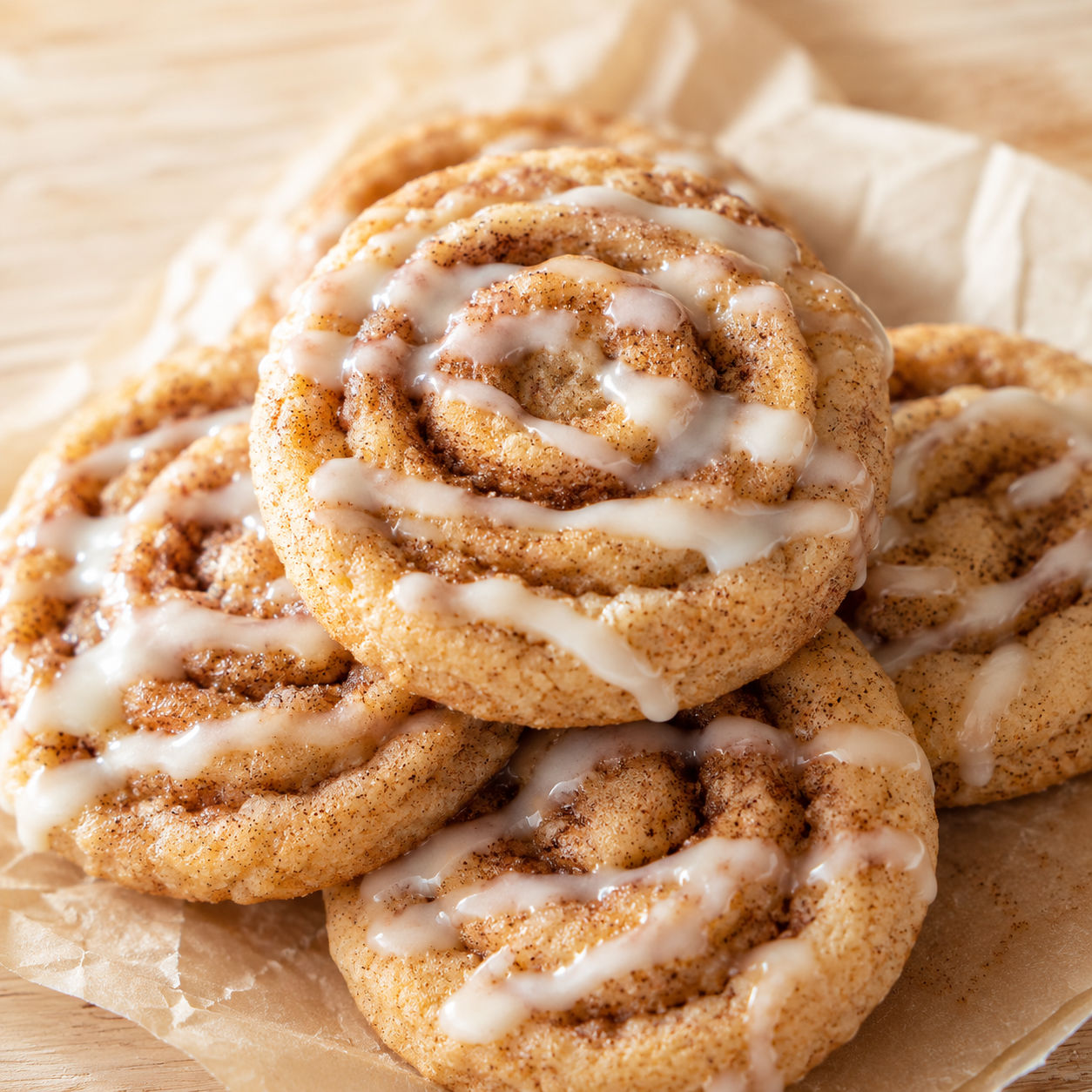 Glazed cinnamon roll cookies with brown sugar swirls on parchment