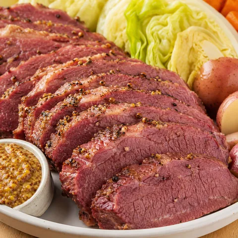Sliced homemade corned beef with potatoes, cabbage, and mustard