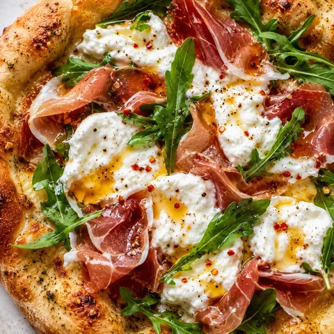 Prosciutto honey burrata pizza with arugula on golden crust