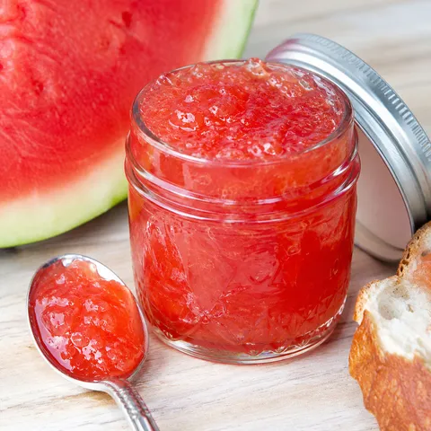 Homemade sweet watermelon jam in a glass jar with a silver spoon on wood
