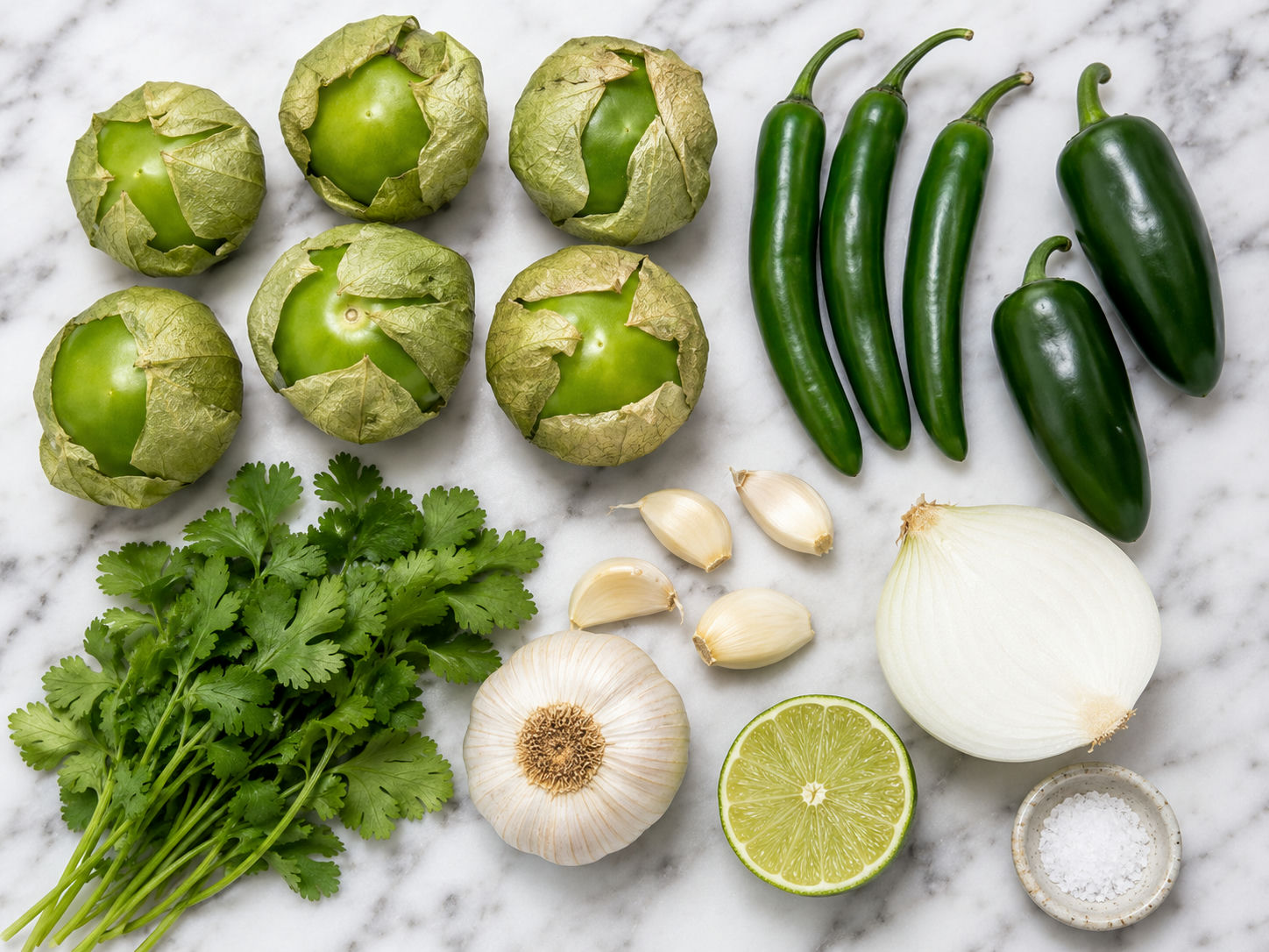 Raw ingredients for salsa pecante: tomatillos, serranos, jalapeños, garlic, cilantro, and lime