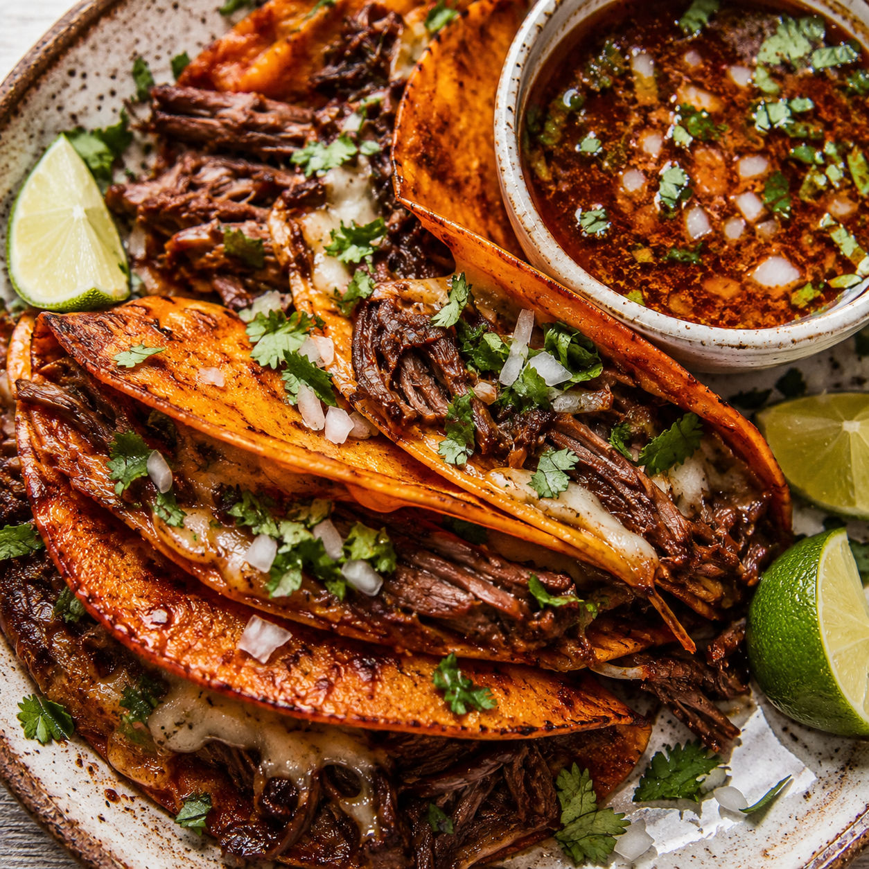 Quesabirria tacos with consomme, cilantro, onion, and lime