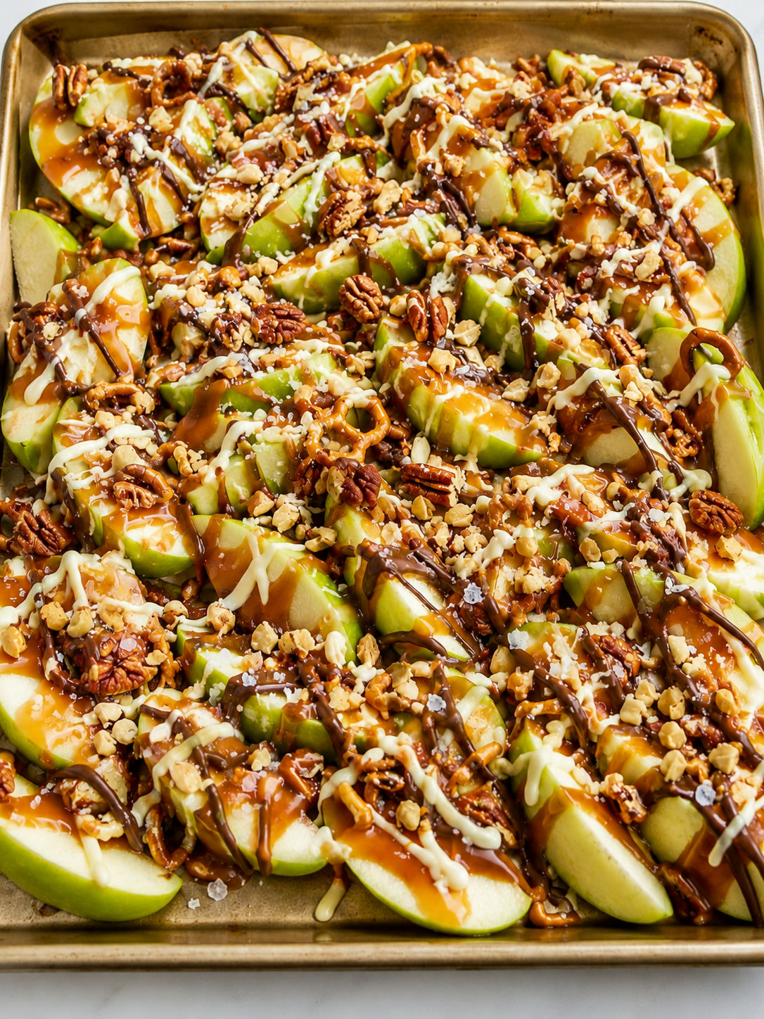 Sheet pan caramel apple slices covered with caramel, chocolate, nuts, and pretzels