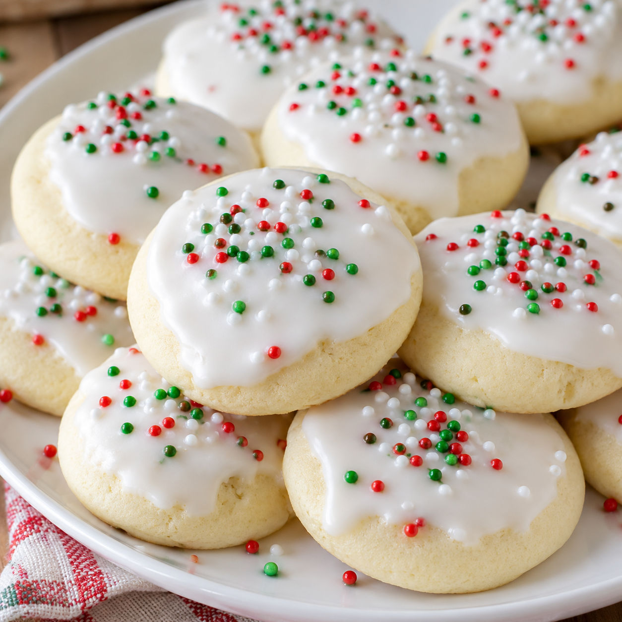 Soft Italian Christmas cookies with white almond glaze and red and green sprinkles on a white plate