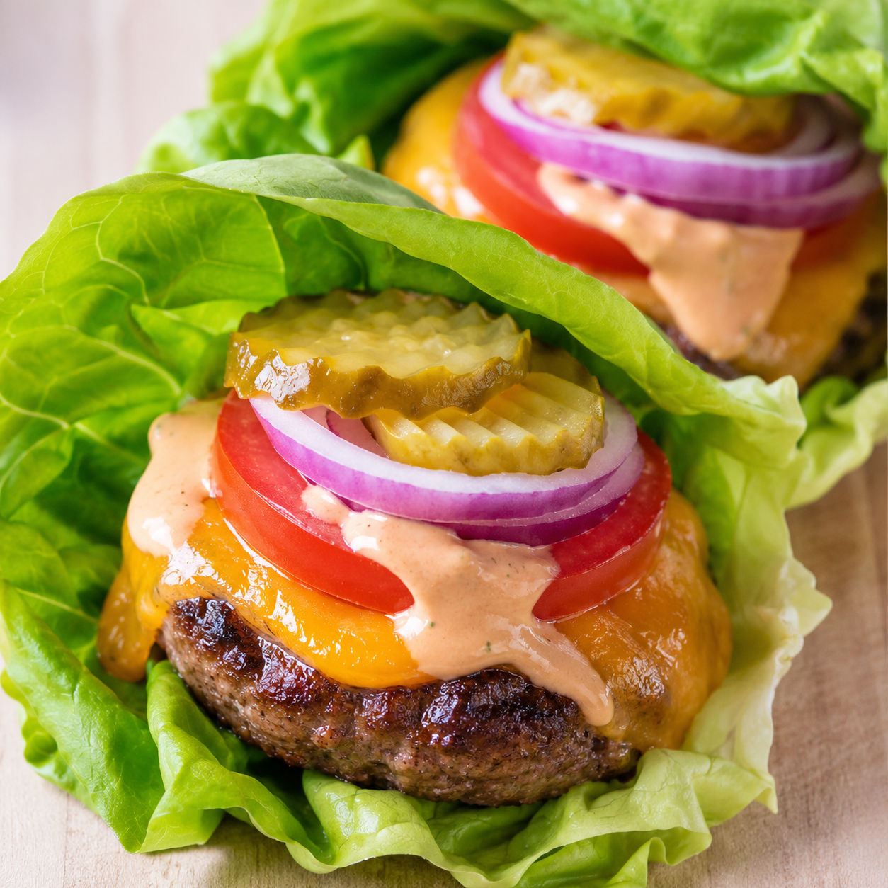 Lettuce wrap burgers with beef patties, cheddar, tomato, pickles, and sauce