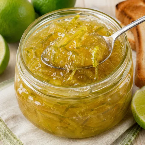 Glossy lime marmalade in a glass jar with toast and fresh limes