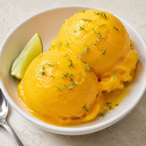 Mango sorbet scoops with lime zest in a white bowl