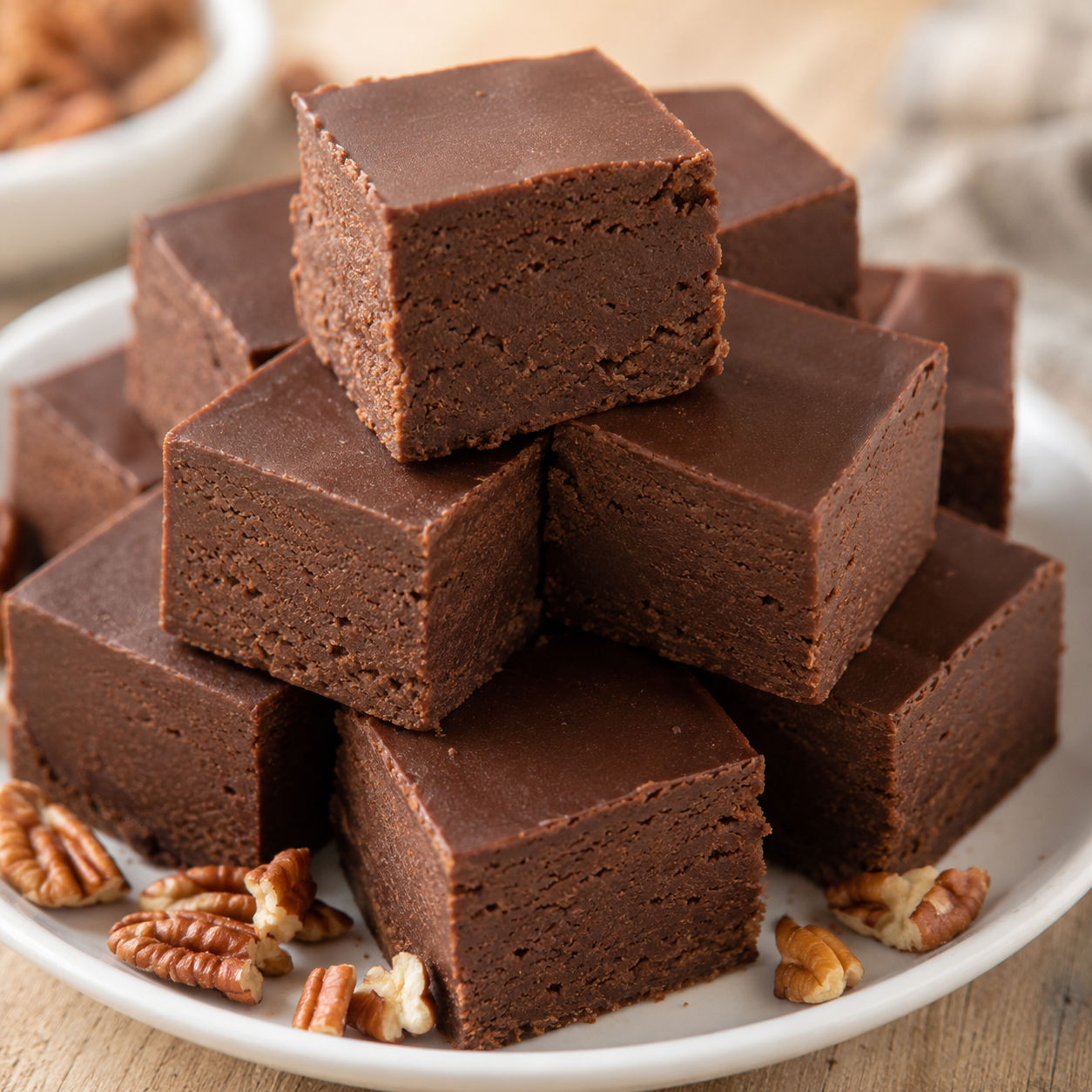 Old Fashioned Fudge squares stacked on a white plate with pecans