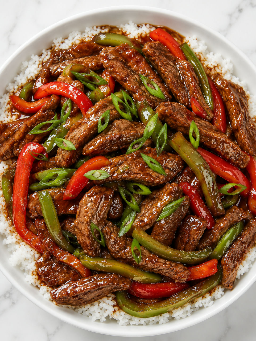 Top-down overhead view of pepper steak with bell peppers over white rice in a white ceramic bowl