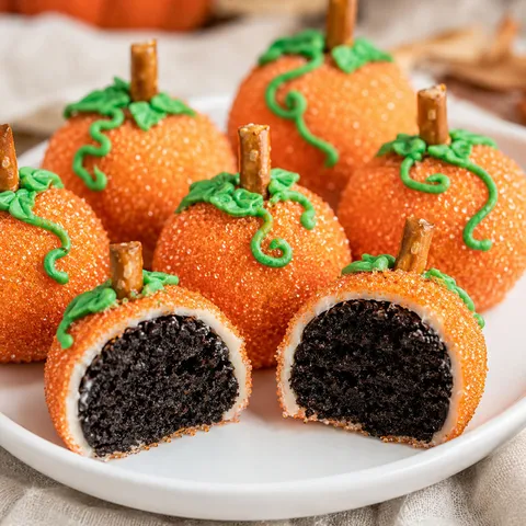 Pumpkin Oreo balls with orange sugar coating and pretzel stems on a white platter