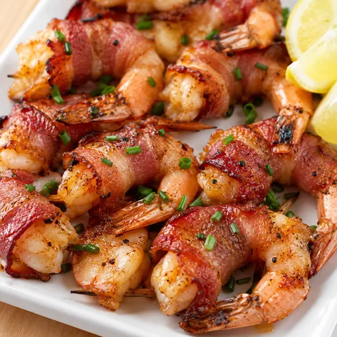 Bacon wrapped shrimp with chives and lemon on a white platter