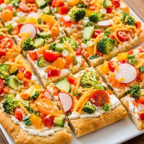 Vegetable pizza appetizer squares with ranch spread and fresh chopped vegetables