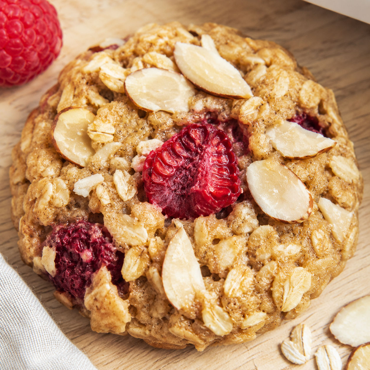 Raspberry almond oat breakfast cookie with oats, raspberries, and sliced almonds on a light wooden surface