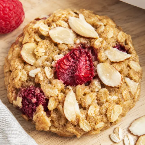 Raspberry almond oat breakfast cookie with oats, raspberries, and sliced almonds on a light wooden surface