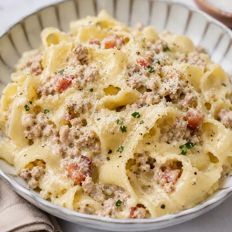 White Bolognese pappardelle with parmesan and herbs in a shallow bowl