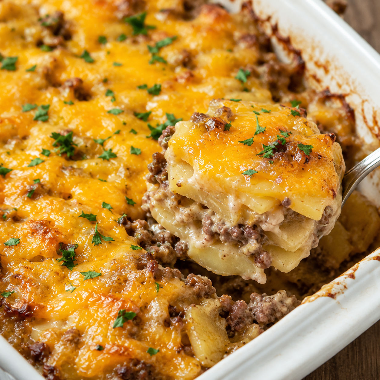 Hamburger potato casserole with melted cheddar and parsley in a baking dish