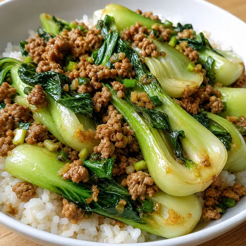 Stir-fried bok choy with ground pork and aromatics in a shallow bowl over rice