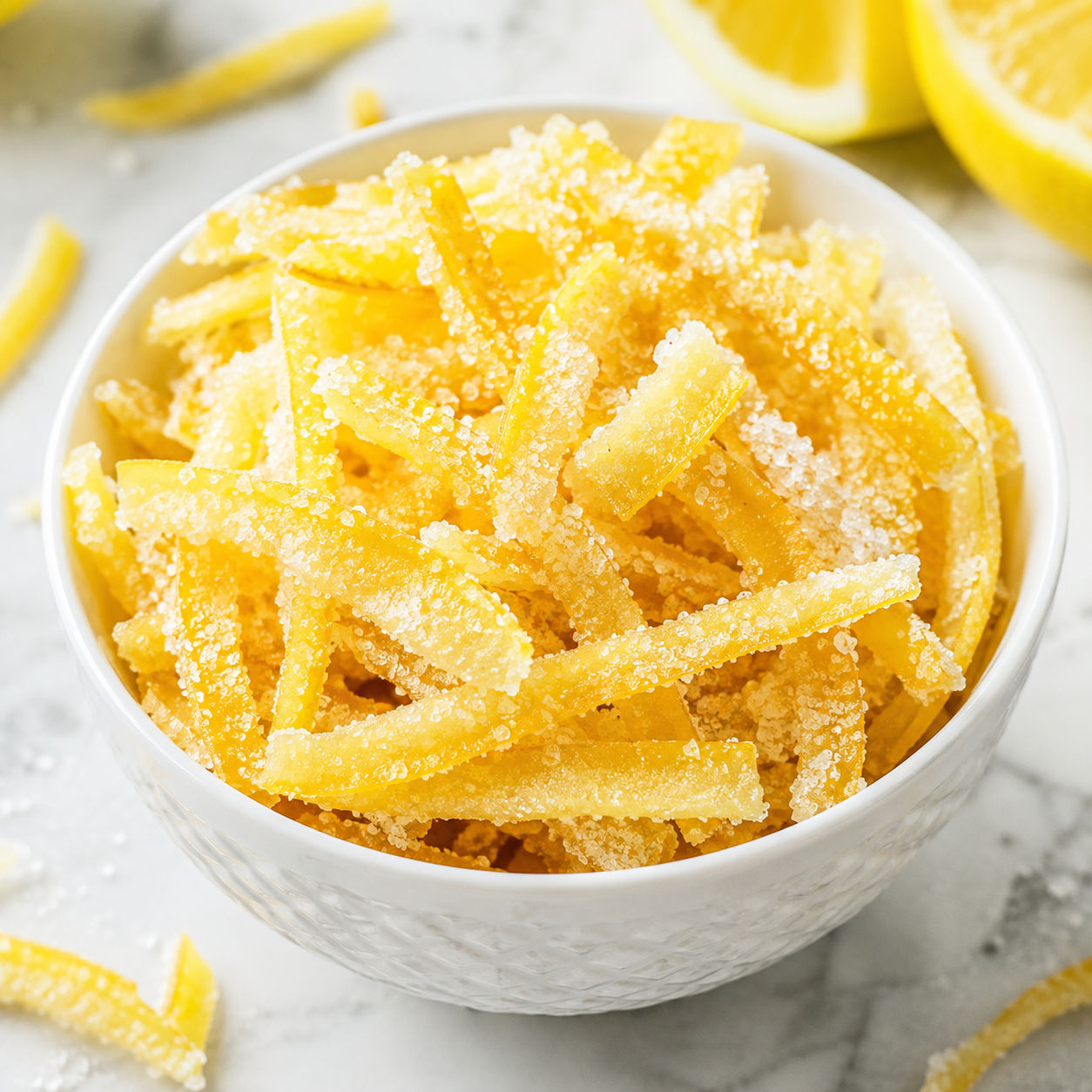 Sugared candied lemon peel strips in a white bowl on parchment
