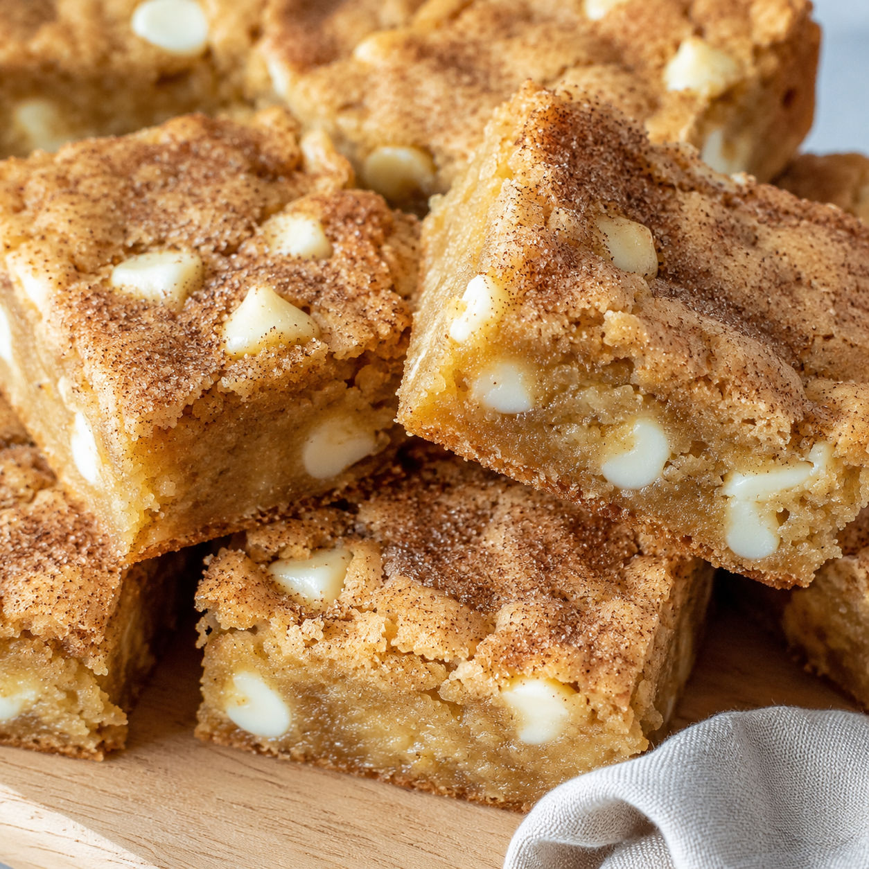 Stack of snickerdoodle blondies with white chocolate chips and crackly cinnamon tops on a wooden board