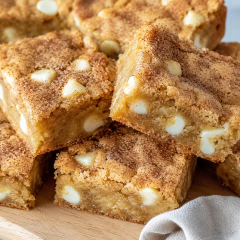 Stack of snickerdoodle blondies with white chocolate chips and crackly cinnamon tops on a wooden board