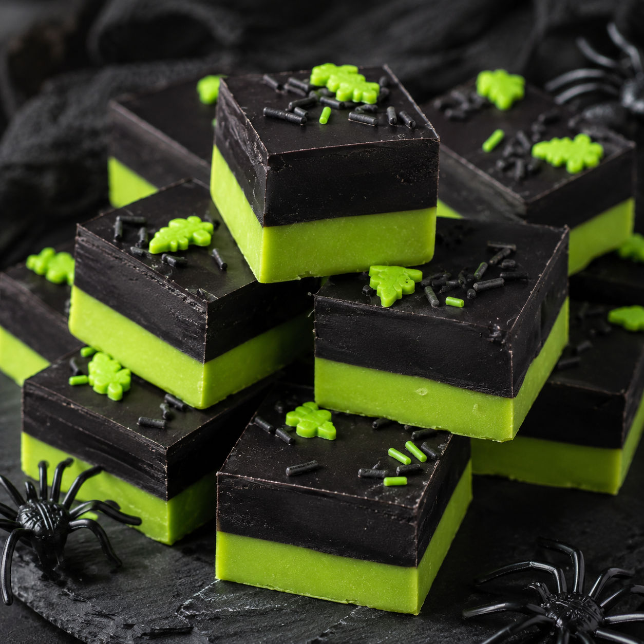 Stacked squares of green and black layered poison apple fudge on dark slate
