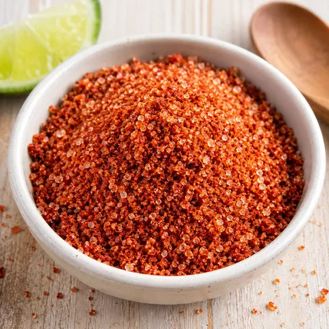 Ruby-red Sriracha Salt in a small white bowl with scattered grains
