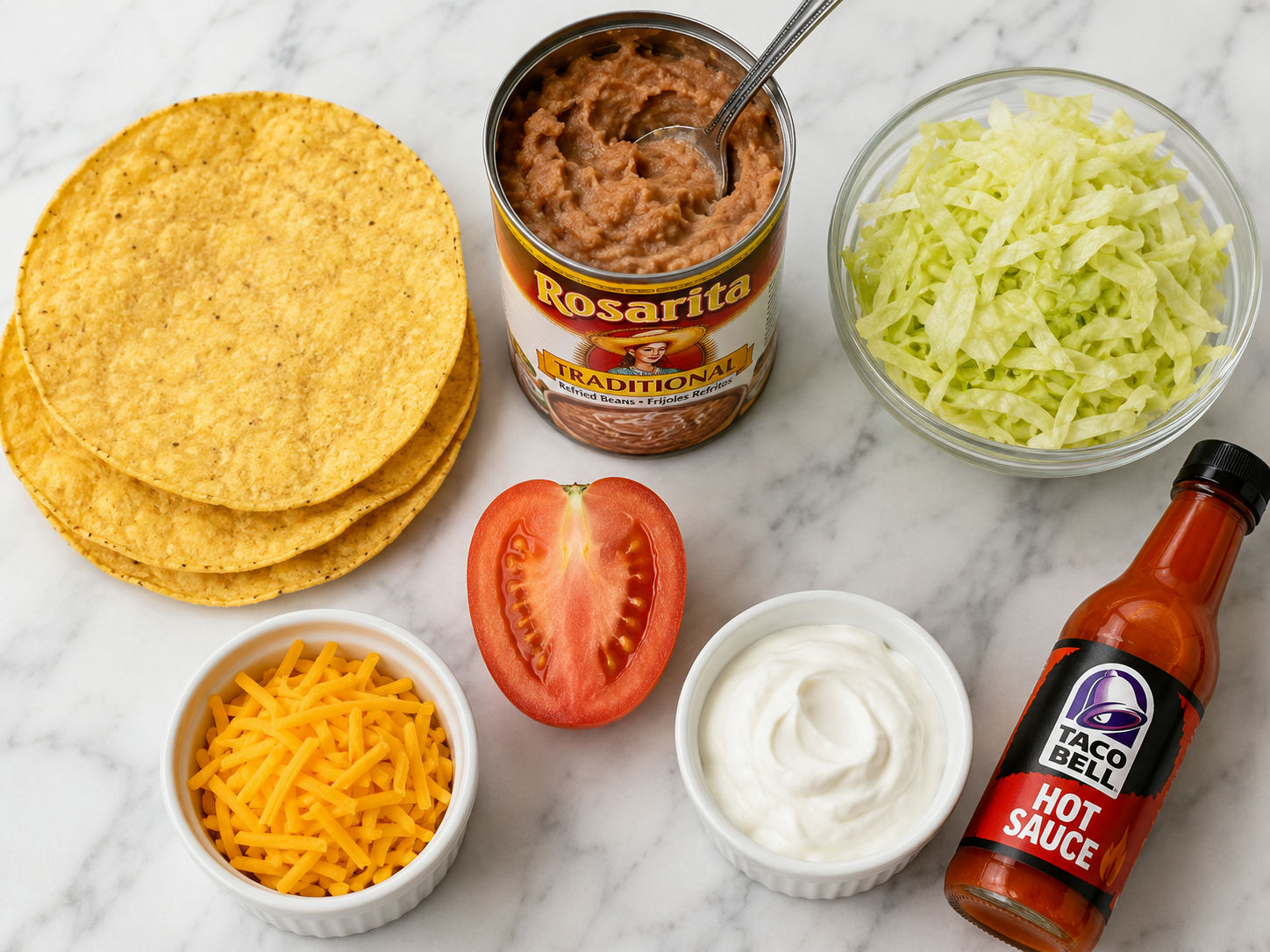 Raw ingredients for Taco Bell tostada copycat including corn shells, refried beans, lettuce, tomato, cheddar cheese, and sour cream on marble