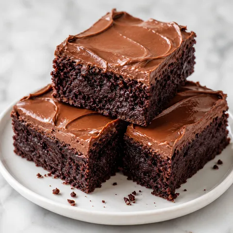 Fudgy brownies with smooth chocolate buttercream stacked on a white plate