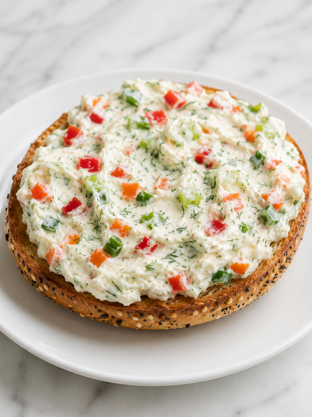 Veggie cream cheese spread on a toasted everything bagel with colorful vegetable flecks