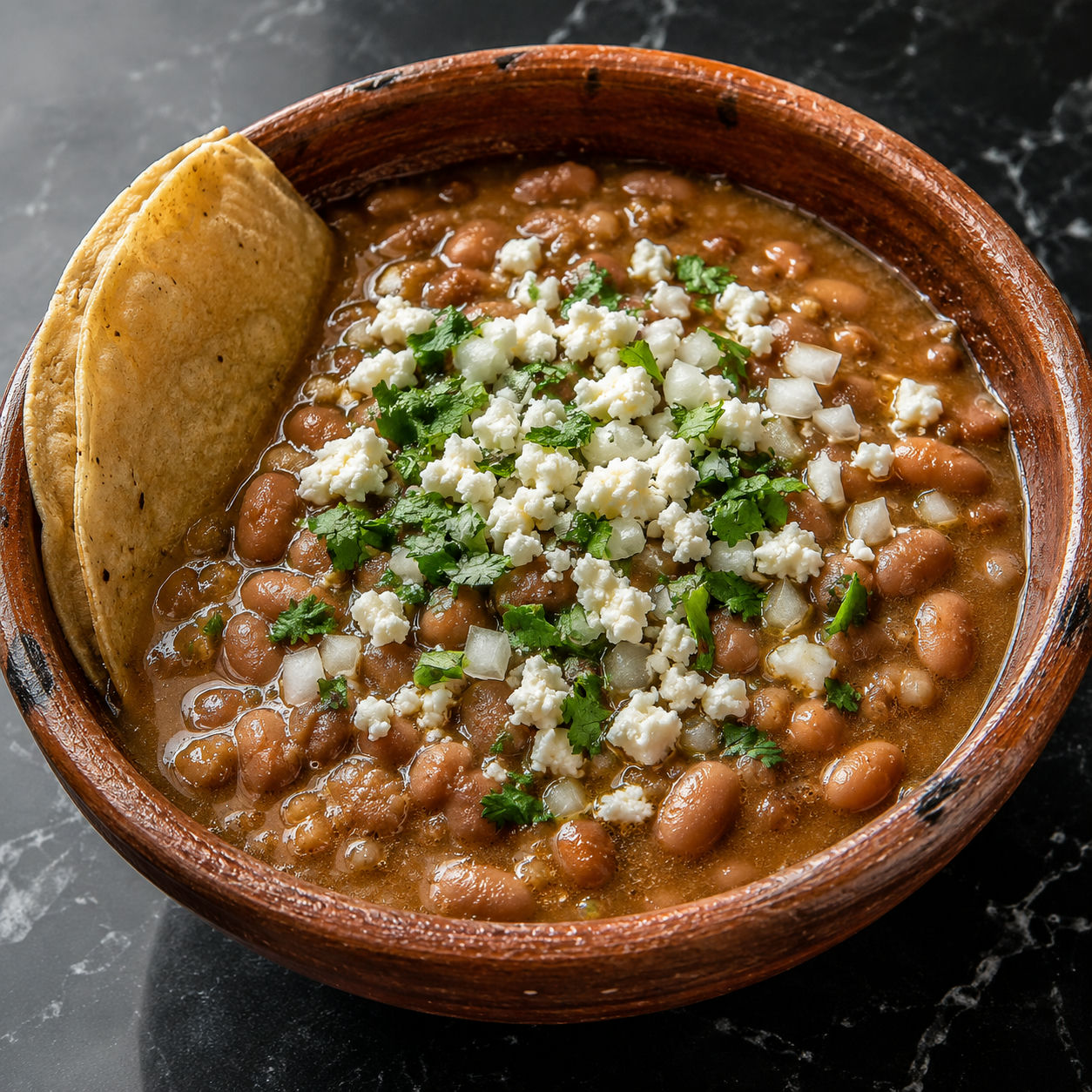 Clay bowl of frijoles de la olla with queso fresco, cilantro, and a corn tortilla