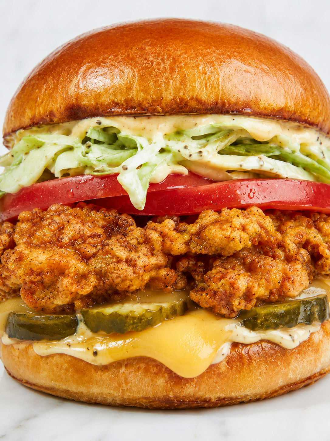Tall crispy chicken sandwich with gouda, pickles, slaw, lettuce, and tomato