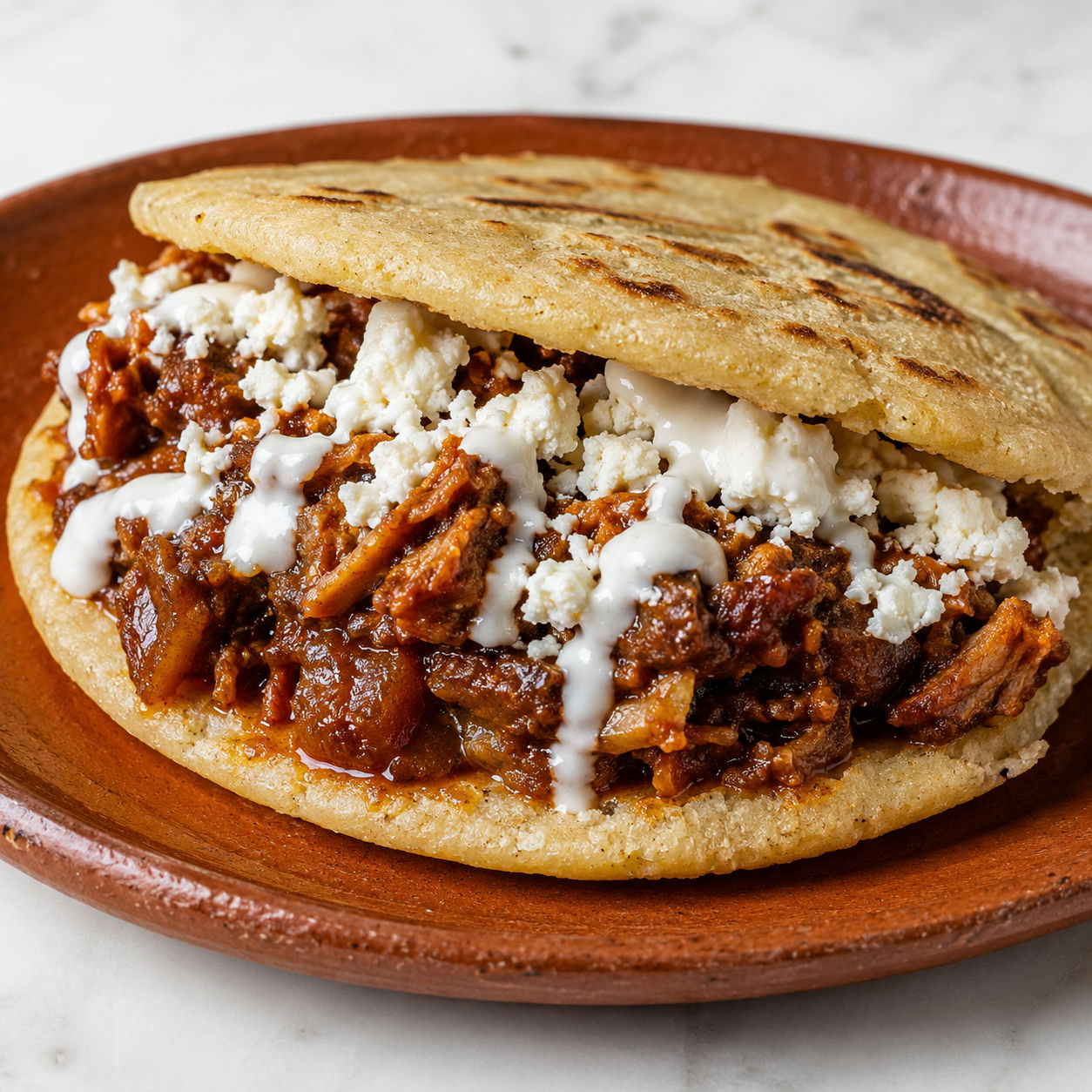 Gordita split open filled with chicharron en salsa and crumbled queso fresco on a clay plate
