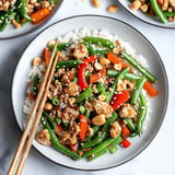 A plate of food with chicken and vegetables, including green beans and peppers, is served with chopsticks.