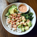 A bowl of rice with avocado and salsa on a wooden table.