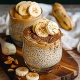 Two glasses of yogurt with bananas and nuts on a table.