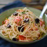 A bowl of pasta with tomatoes and olives.