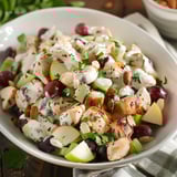 A bowl of food with grapes, chicken, and other vegetables.