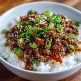 A bowl of rice with meat and vegetables, including peppers and onions, in a sauce.