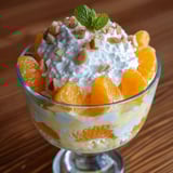 A bowl of orange dessert with white cream and nuts.