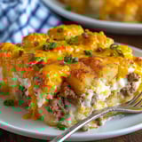 A delicious tater tot casserole with cheese and potatoes, served on a white plate.