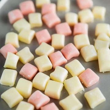 A plate scattered with small, pastel-colored square candies in pink and yellow.