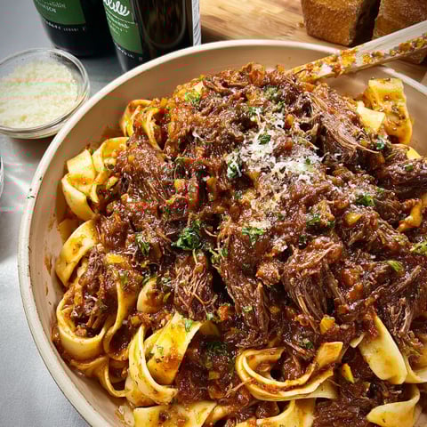 A delicious Slow-Cooked Short Rib Ragu is served in a bowl, garnished with fresh herbs and spices.