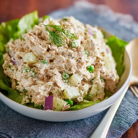 A bowl of tuna salad with lettuce and onions, served on a wooden table.
