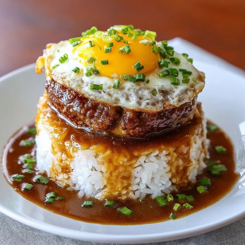 A delicious Hawaiian Loco Moco dish, featuring a fried egg on top of a bed of rice, is served on a white plate.