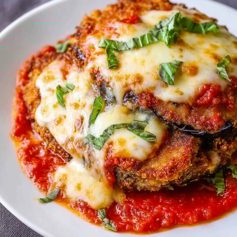 A delicious Chicken Eggplant Parmesan dish is served on a white plate.