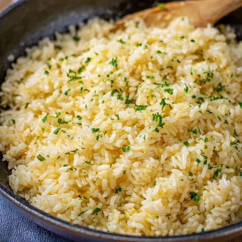 A bowl of rice with green herbs on top, likely garlic butter rice.