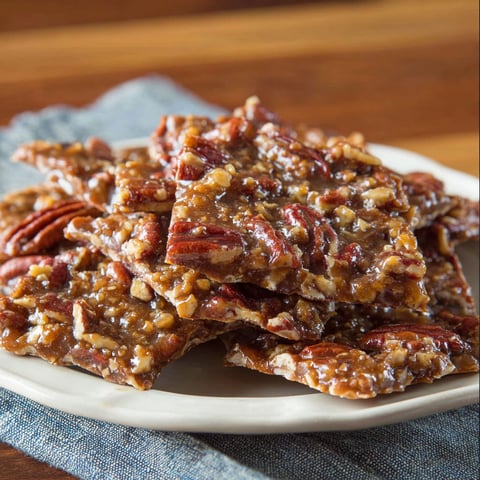 A plate of pecan pie bark is displayed on a wooden table.