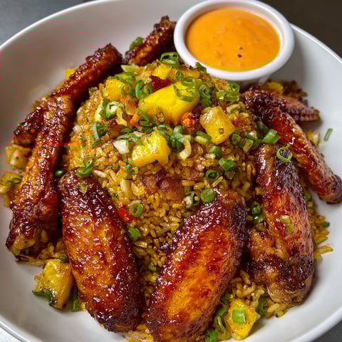 A plate of fried rice with chicken, bacon, and pineapple, topped with a spicy yum yum sauce.